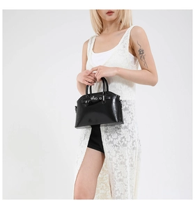 Detail of black glossy patent leather handbag with silver buckles and dual top handles