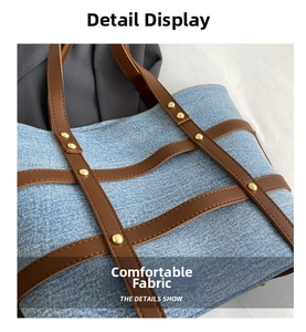 Close-up of light blue denim tote bag with brown leather accents and gold rivets