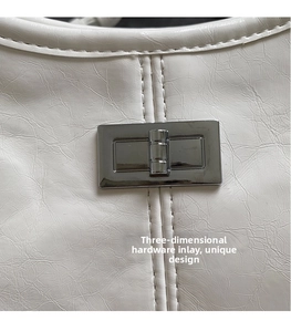 Close-up of silver metal clasp on white pleated patent leather shoulder bag with stitching