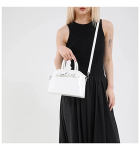 Detail of a white glossy shell crossbody bag with silver buckle and thin strap