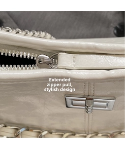 Detailed view of ivory pleated patent leather bag with silver zipper and chain strap