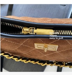 Detail of smooth gold zipper and brown suede quilted texture on a chain shoulder bag
