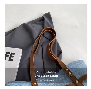 Detail of light blue denim tote bag with brown leather strap and golden rivet reinforcement