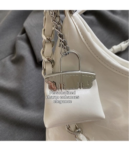 Detail of white glossy wrinkled leather shoulder bag with a mini charm and silver chain