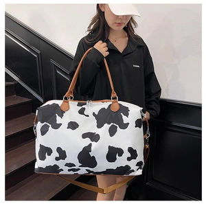 Detail of cow print travel bag featuring leather handles and adjustable shoulder strap
