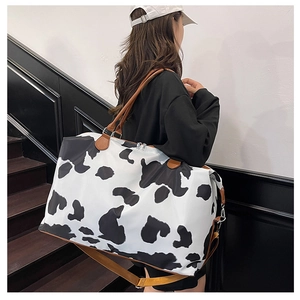 Detailed side view of cow print travel bag featuring brown leather straps and handles