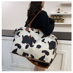 Detail shot of a cow print travel bag with leather handles and adjustable shoulder strap