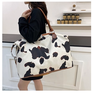 Close-up of a large cow print travel bag with brown faux leather handles and metal hooks