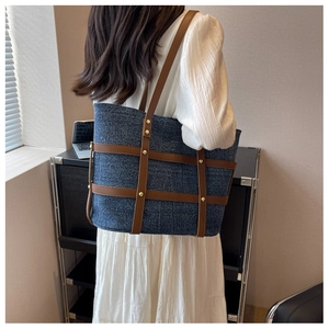 Detail view of retro denim tote bag with leather trim and rivet accents on a model