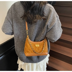 Back view of brown quilted suede underarm bag with gold chain on model in stylish room