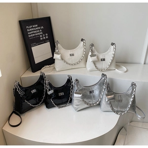 Detailed view of three glossy crescent bags with chain straps on a white tiered display