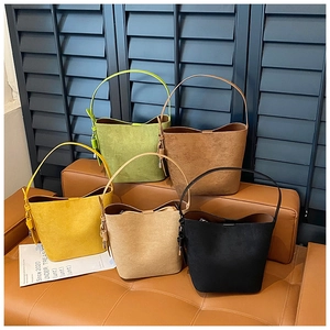 Close-up of five colorful matte suede bucket bags arranged on a leather stool