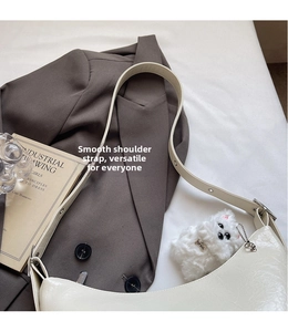 Close-up of white glossy patent leather hobo bag with adjustable strap and plush puppy charm