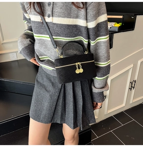 Detail of black suede quilted crossbody bag with golden dual zippers and charms