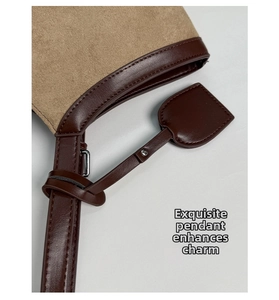 Detailed close-up of khaki suede tote with leather trim and shield-shaped charm