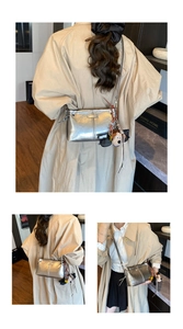 Drie weergaven van een metallic zilveren crossbodytas met stiksels en bedeltje