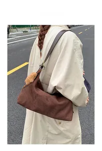 Close-up of suede crossbody bag featuring a plush ball charm and leather strap detailing