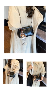 Detail van zwarte glanzende crossbodytas met pluche puppy-bedel en modieus logo