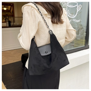 Detail of minimalist black tote bag with suede texture and metal chain strap on model