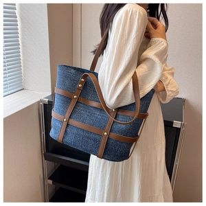 Close-up of denim tote bag with brown leather straps and gold rivets on a model