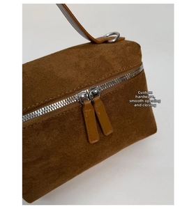Détail des doubles fermetures éclair argentées et du matériel sur un sac en daim marron