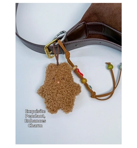 Brown fluffy bear plush charm with colorful beads on a leather bag strap detail