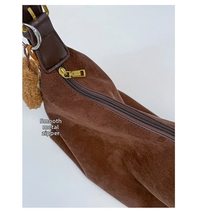 Detail of smooth golden metal zipper on brown suede handbag with plush ball pendant