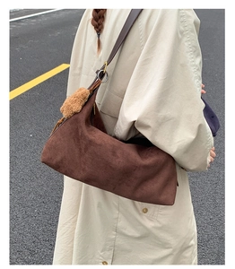 Brown frosted suede baguette bag with leather strap and plush ball detail shown on a person