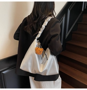 Sac hobo argenté avec bandoulière froissée et breloque ours porté par un modèle