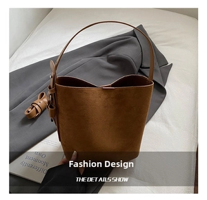 Detail of a brown matte suede bucket bag with adjustable side strap on a neutral fabric