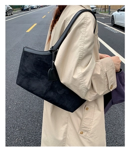 Detail of a large black matte leather tote bag worn with a casual beige trench coat