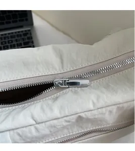 Close-up of smooth silver zipper on off-white nylon tote bag with office background