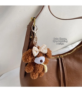 Porte-clés chien en peluche marron avec nœud à carreaux sur un sac à bandoulière en cuir