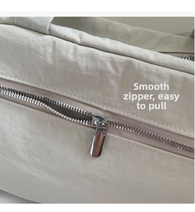 Detail of a smooth silver metal zipper on a minimalist beige nylon tote shoulder bag
