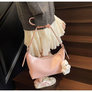 Pink glossy faux leather shoulder bag with plush dog charm on wooden stairs