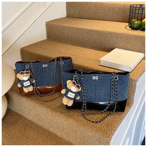 Detail view of denim tote bag with leather contrast and plush teddy bear accessory