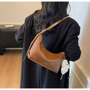 Detail of brown crescent shoulder bag with oil wax texture and white plush pendant