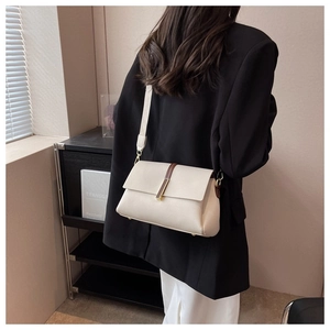 Detail of off-white lychee grain leather crossbody bag with brown accent and gold buckle