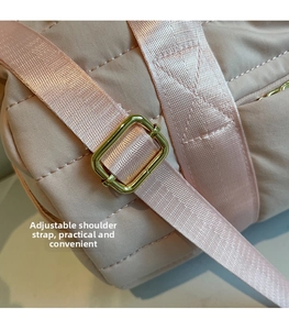 Detail of light pink quilted bag featuring adjustable shoulder strap and gold metal buckle