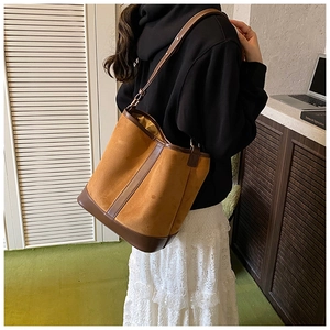 Close-up of caramel matte suede bucket bag with dark brown leather trim on female model