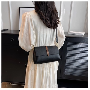 Detail of black lychee grain leather crossbody bag with gold buckle and brown leather accent