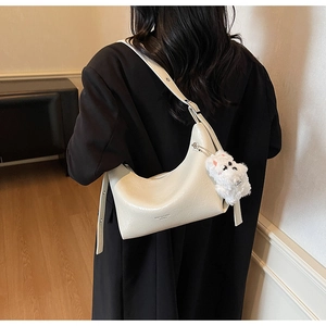 Detail of cream white patent leather crescent bag with plush puppy charm and pleated texture