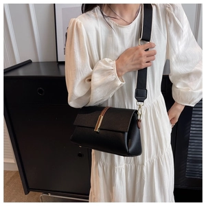 Detail of black pebbled leather crossbody bag with wide strap and gold metal buckle