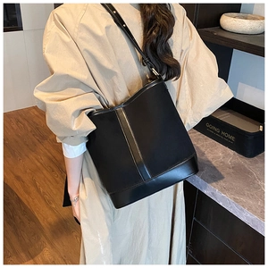 Detail of a black canvas and leather bucket bag worn with a classic beige trench coat