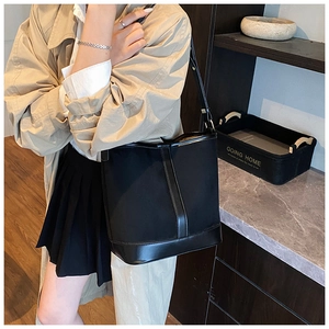 Side view of a vintage black bucket bag made of fabric and leather on a stylish female model