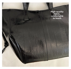 Close-up of black glossy tote bag showing parallel stitching and smooth leather texture