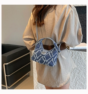Dettaglio della borsa in denim blu con frange rovinate e cuciture bianche a diamante