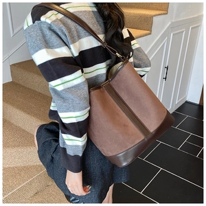 Detail of a large brown faux suede bucket bag with contrast leather trim on a model