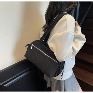 Detail of a minimalist black nylon tote bag with silver zipper on a model's shoulder