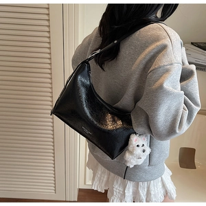 Detail of black leather hobo bag with a plush puppy charm and adjustable strap
